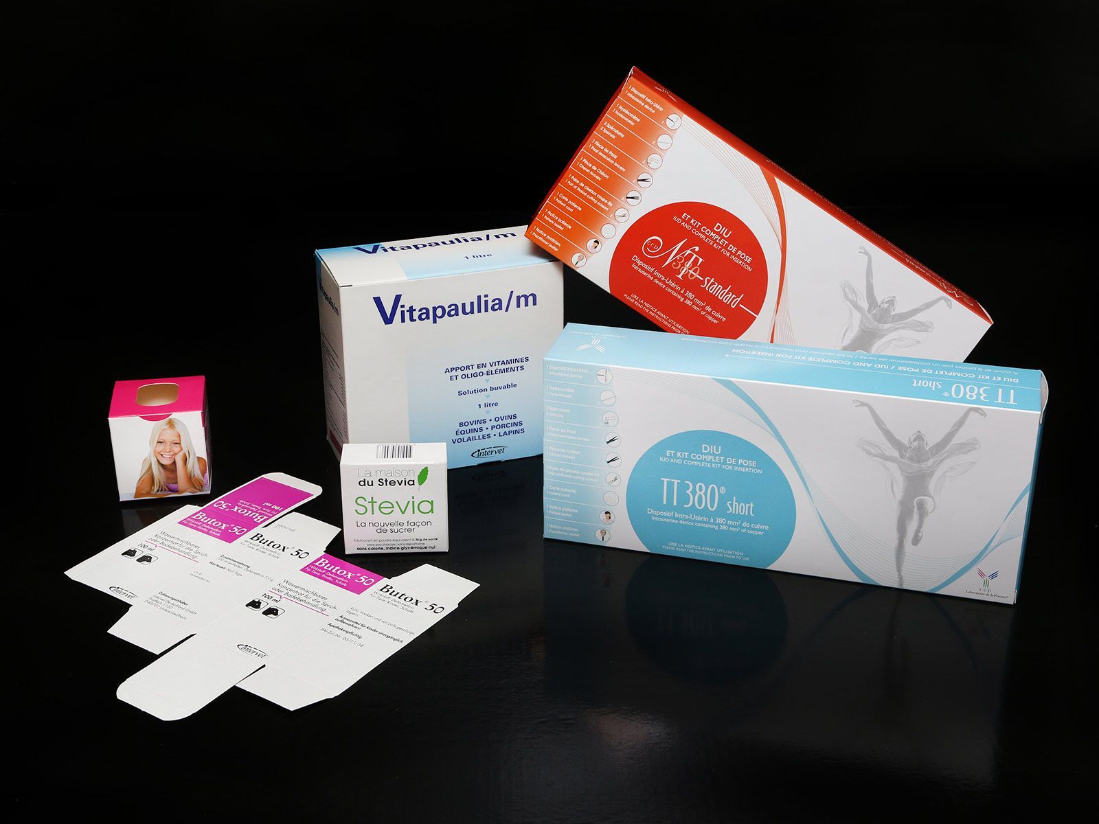 Plusieurs boîtes de produits colorées sur une surface noire réfléchissante, probablement pour des vitamines ou des compléments alimentaires.