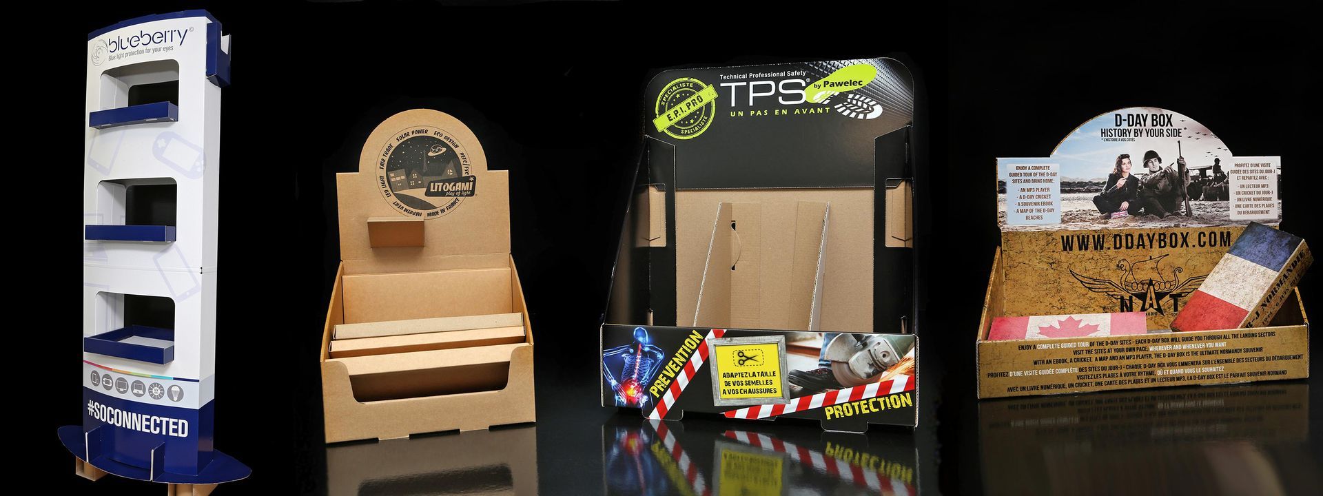 Quatre présentoirs en carton de produits différents sur fond noir.