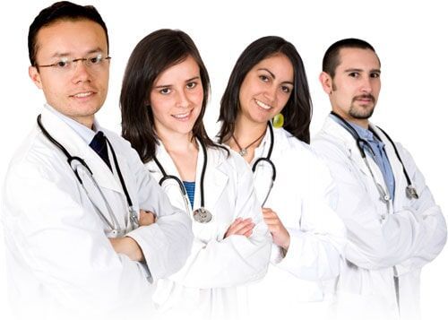 Grupo de quatro médicos de jaleco branco, sorrindo, com estetoscópios em volta do pescoço, braços cruzados