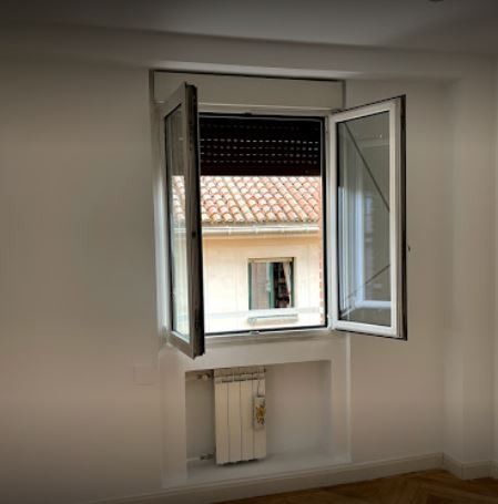 Ventana blanca de guillotina con vistas a los tejados. Un radiador se encuentra debajo de la ventana, en un nicho empotrado.