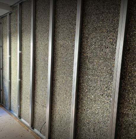 Vista interior de un muro en construcción, que muestra la estructura metálica y el aislamiento entre los montantes. El aislamiento presenta una apariencia moteada y texturizada.