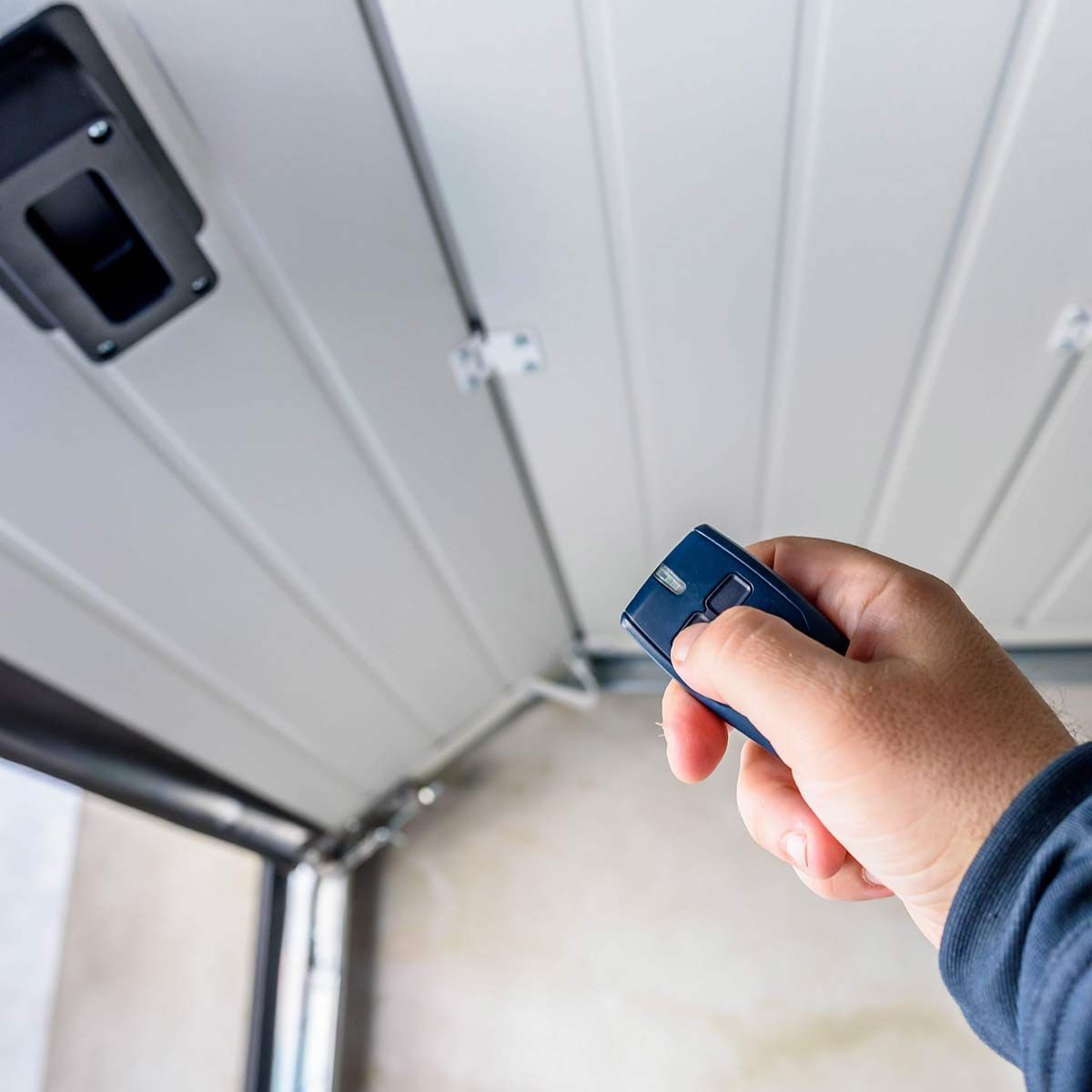 Main qui tient une télécommande devant une porte de garage déroulante