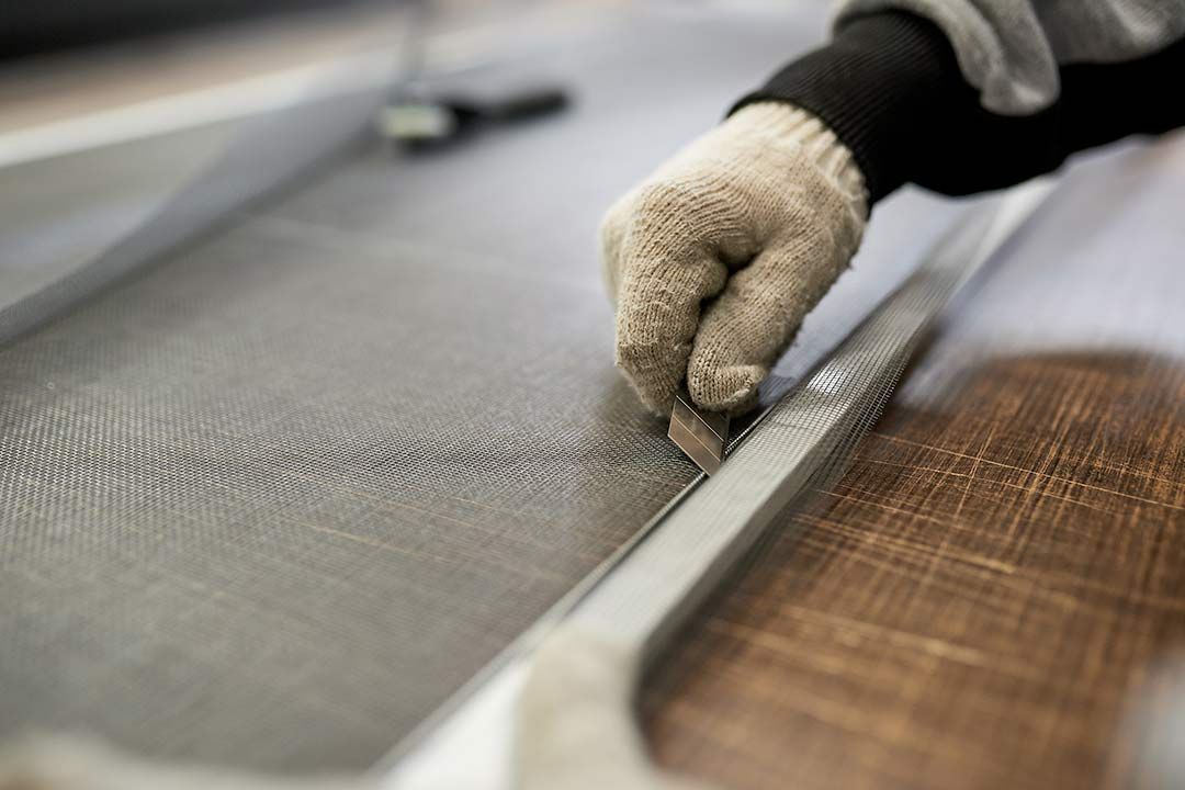 Main qui découpe un moustiquaire avec un cutter