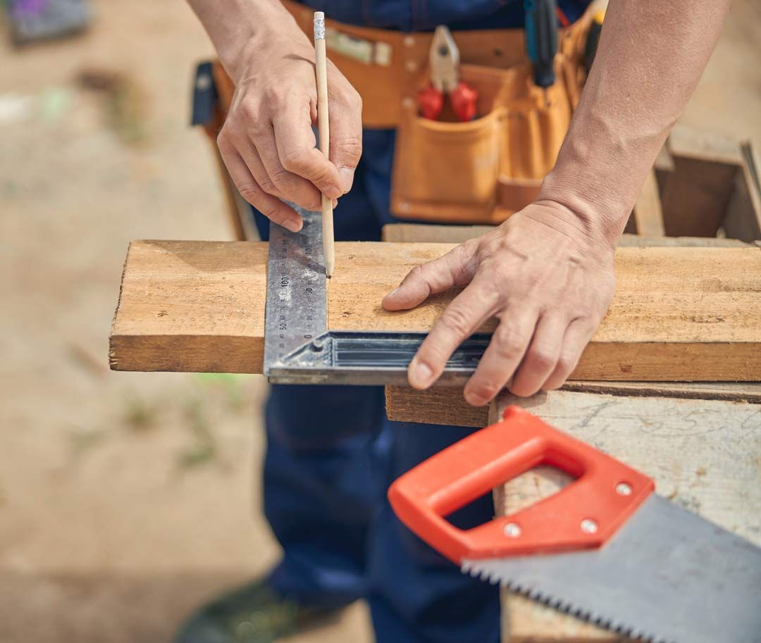 Mains traçant une mesure sur une planche en bois à l'aide d'une règle et d'un crayon
