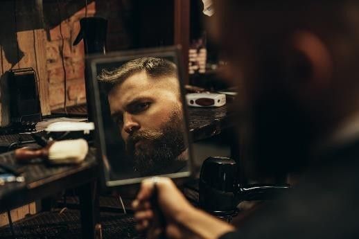 Homme qui se regarde dans un mirroir avec sa barbe taillée