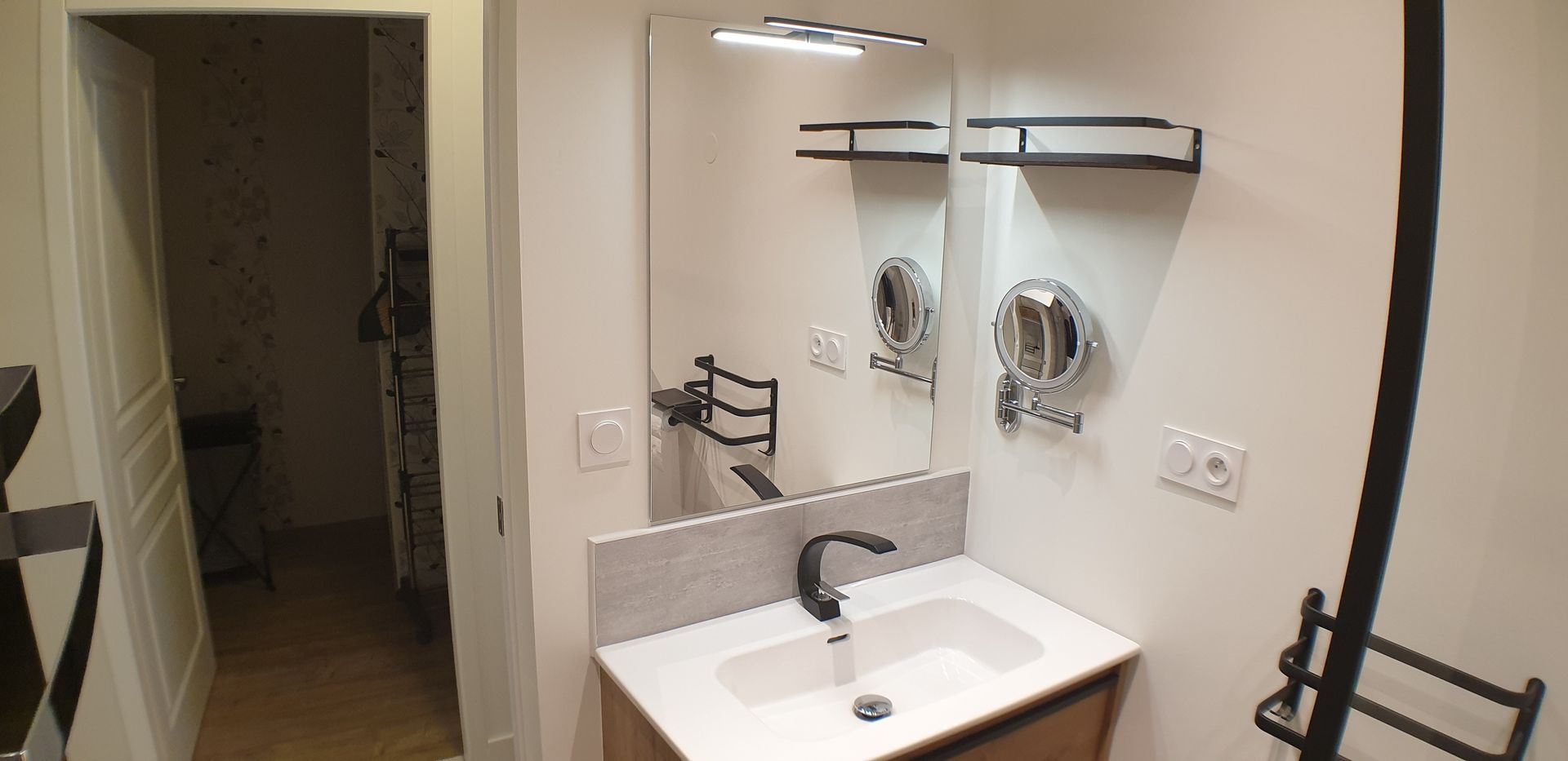 Salle de bains moderne avec un miroir lumineux et des étagères noires