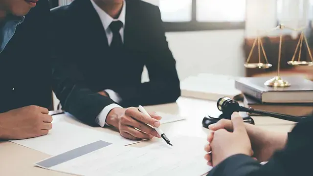 Personas con traje revisando documentos en una mesa, con un mazo, libros de leyes y una balanza de la justicia en el fondo.