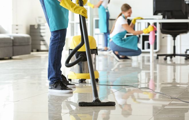 Reinigungskräfte säubern einen glänzenden Büroboden mit Mopp und Staubsauger.