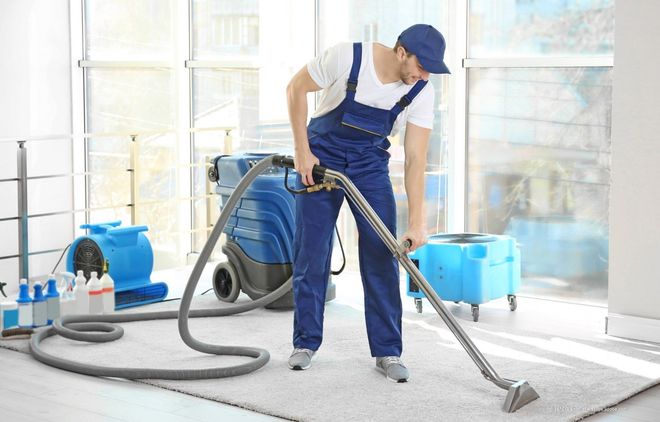 Ein Arbeiter saugt mit einem großen Industriesauger den Boden eines hellen Zimmers.