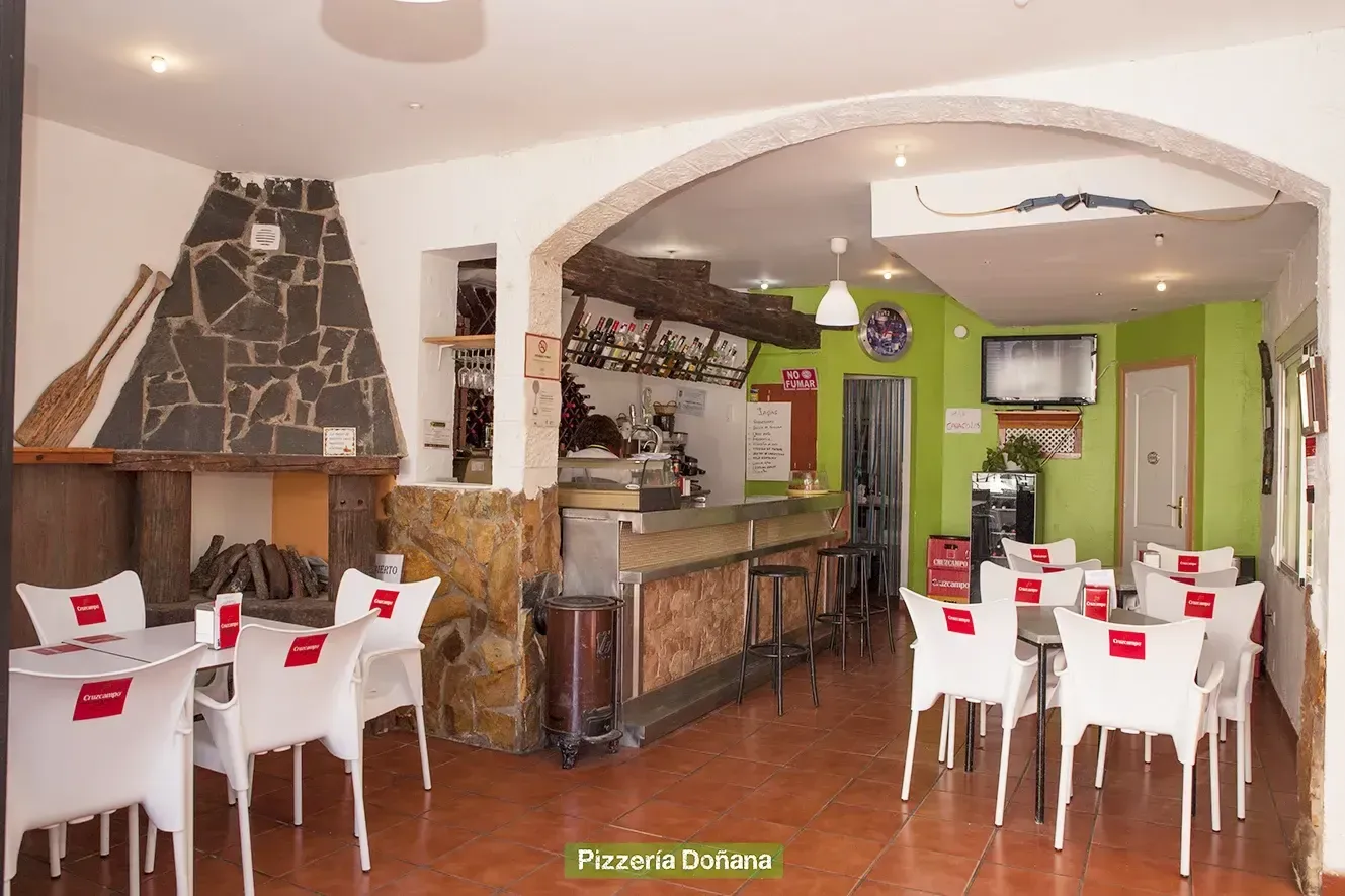 El interior de un restaurante rústico cuenta con una chimenea de piedra, una barra de servicio y varias sillas.