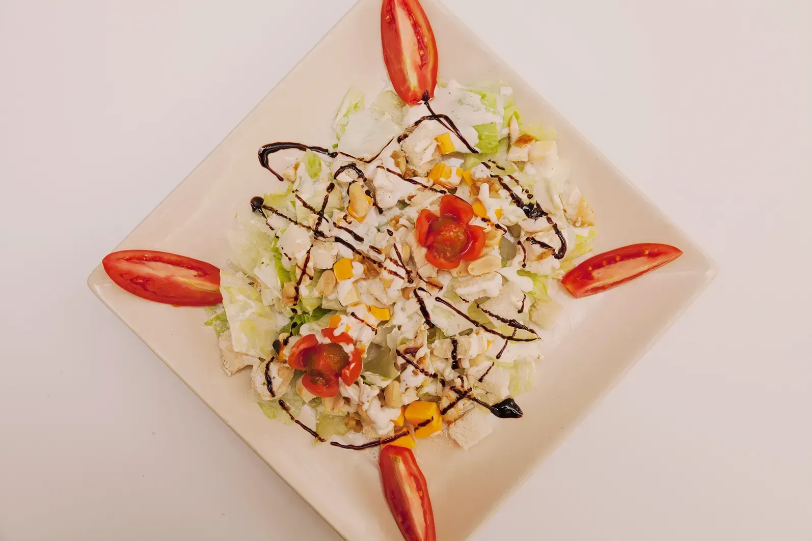 Una ensalada servida en un plato cuadrado blanco, aderezada con glaseado balsámico y adornada con cuatro gajos.