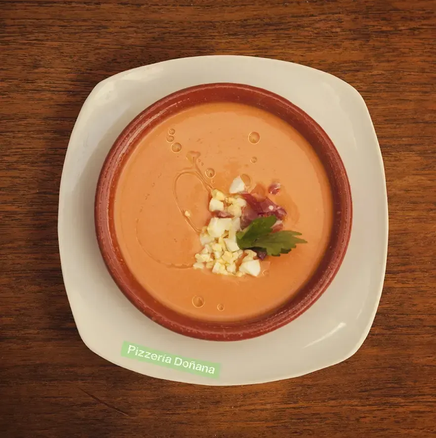 Un cuenco de barro con salmorejo, cubierto con huevo picado, jamón serrano y aceite de oliva.
