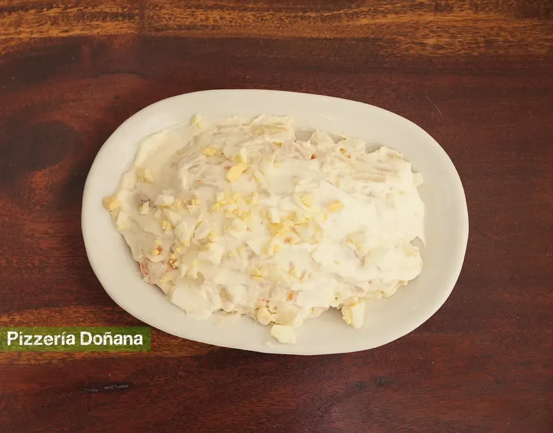 Un plato ovalado blanco con una ensalada de patatas cremosa coronada con pequeños trozos de huevo.