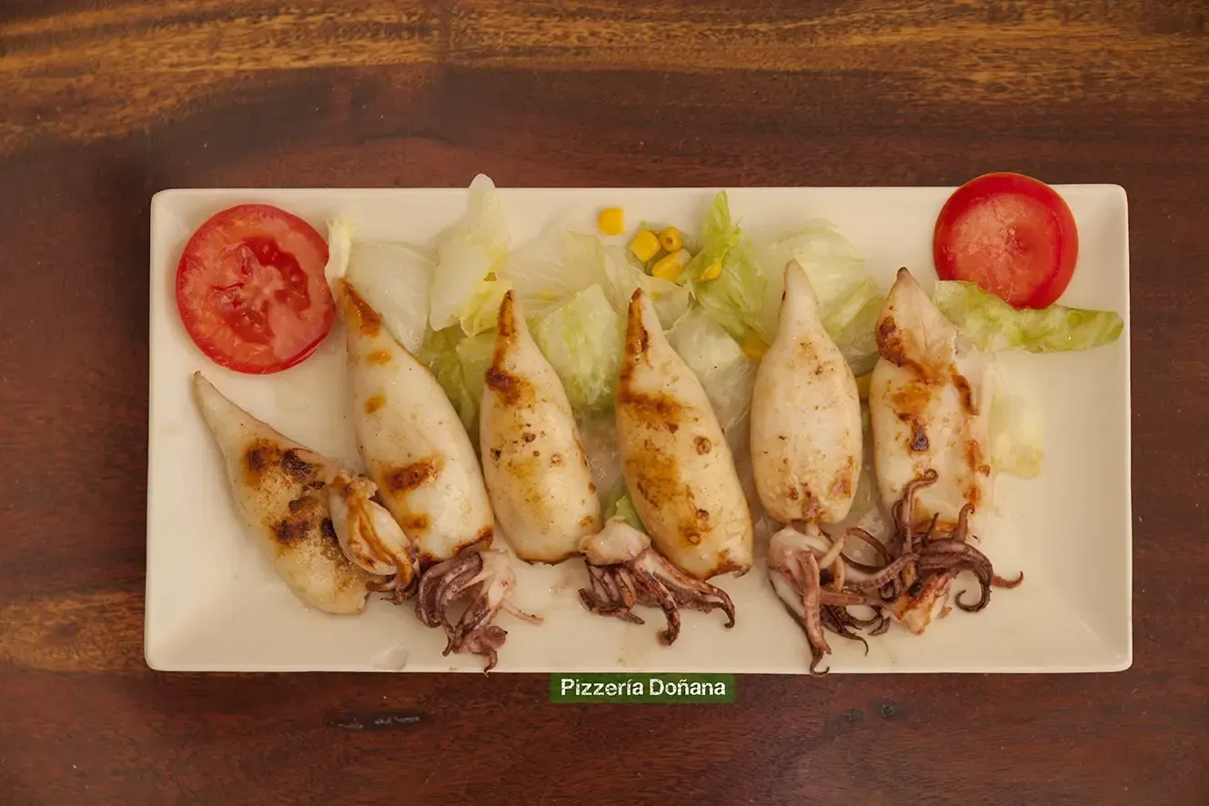 Seis calamares enteros a la parrilla, dispuestos en un plato rectangular blanco con lechuga.