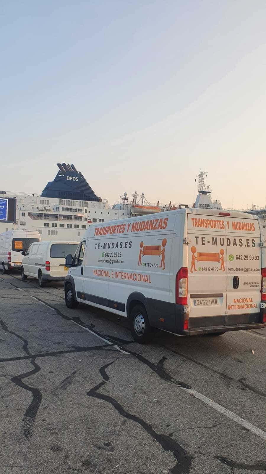 Furgonetas blancas de servicio con letras rojas estacionadas en una carretera agrietada al anochecer, cerca de una costa rocosa.