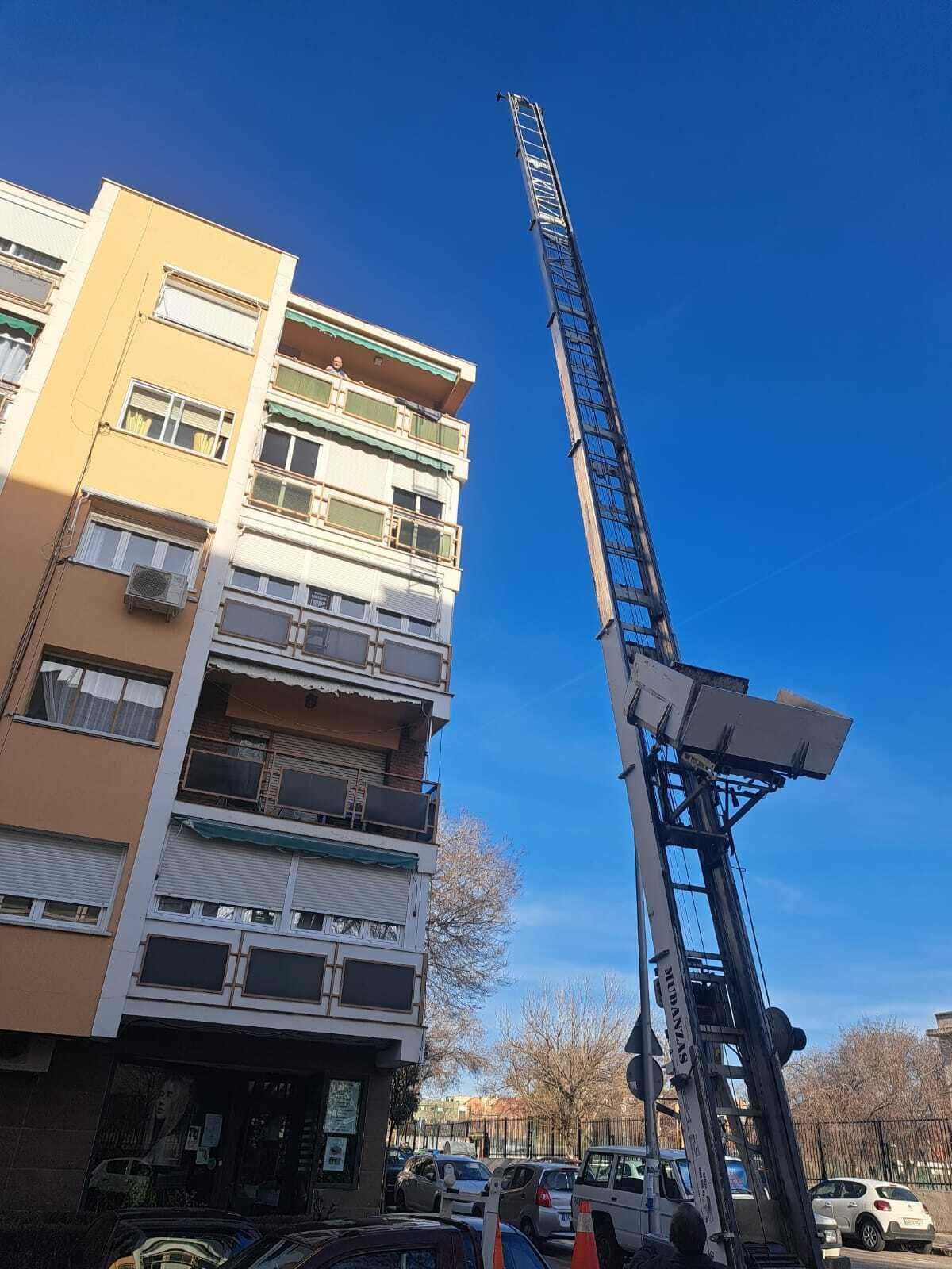 Grúa de construcción alta junto a un edificio de apartamentos en una calle soleada bajo un cielo azul despejado.