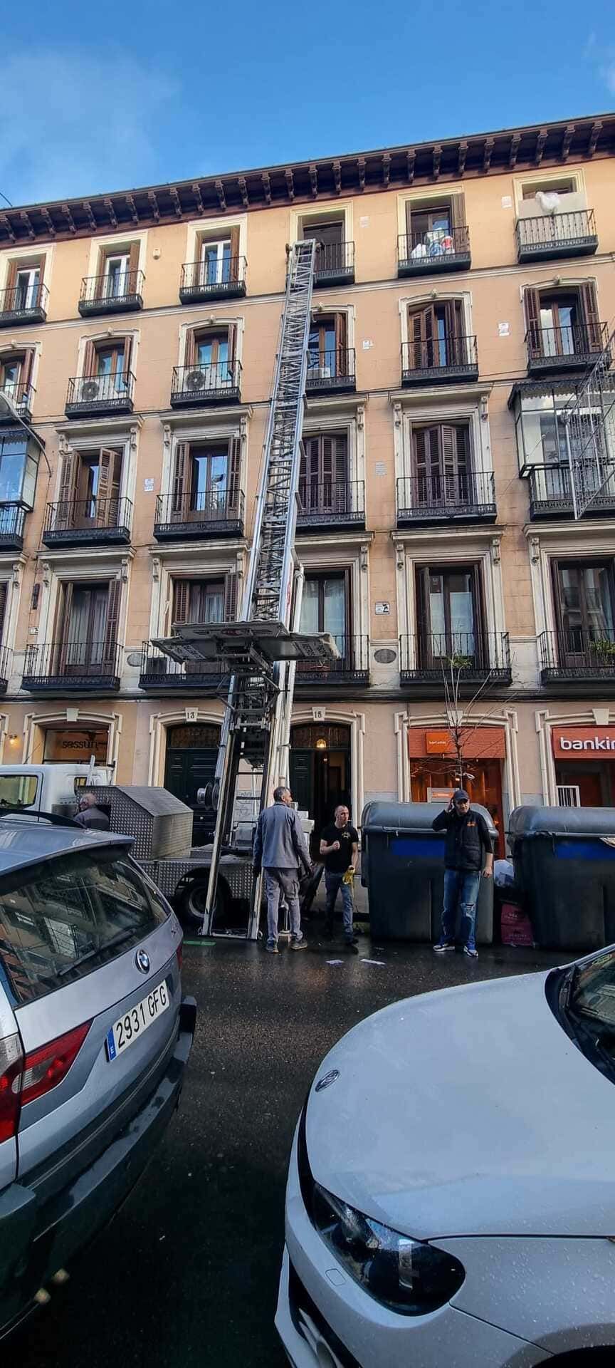 Vista de la calle de un edificio de apartamentos beige con balcones y coches aparcados delante.