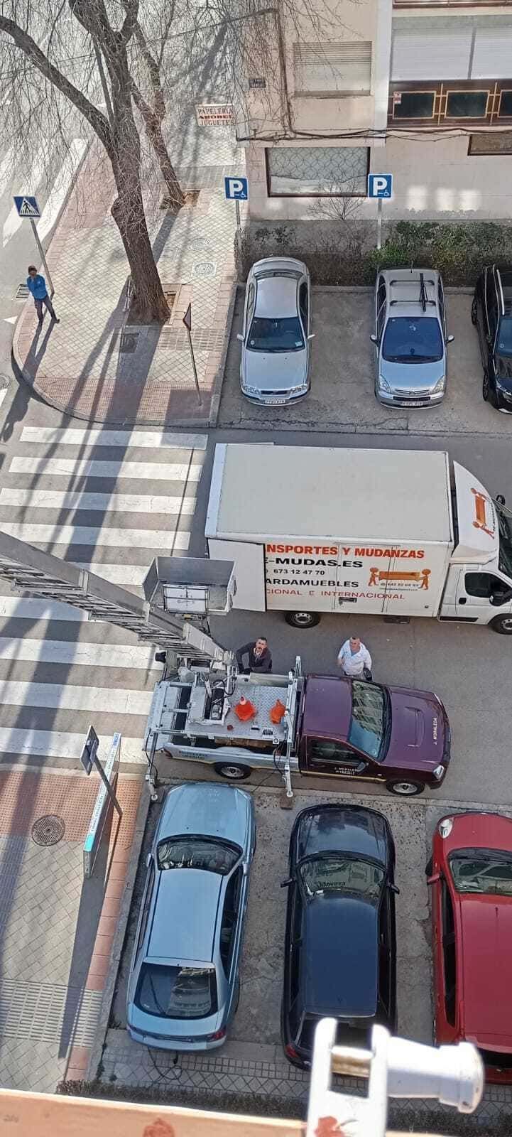 Vista aérea de un estacionamiento con varios autos estacionados y una camioneta blanca, además de peatones cerca de la parte inferior.