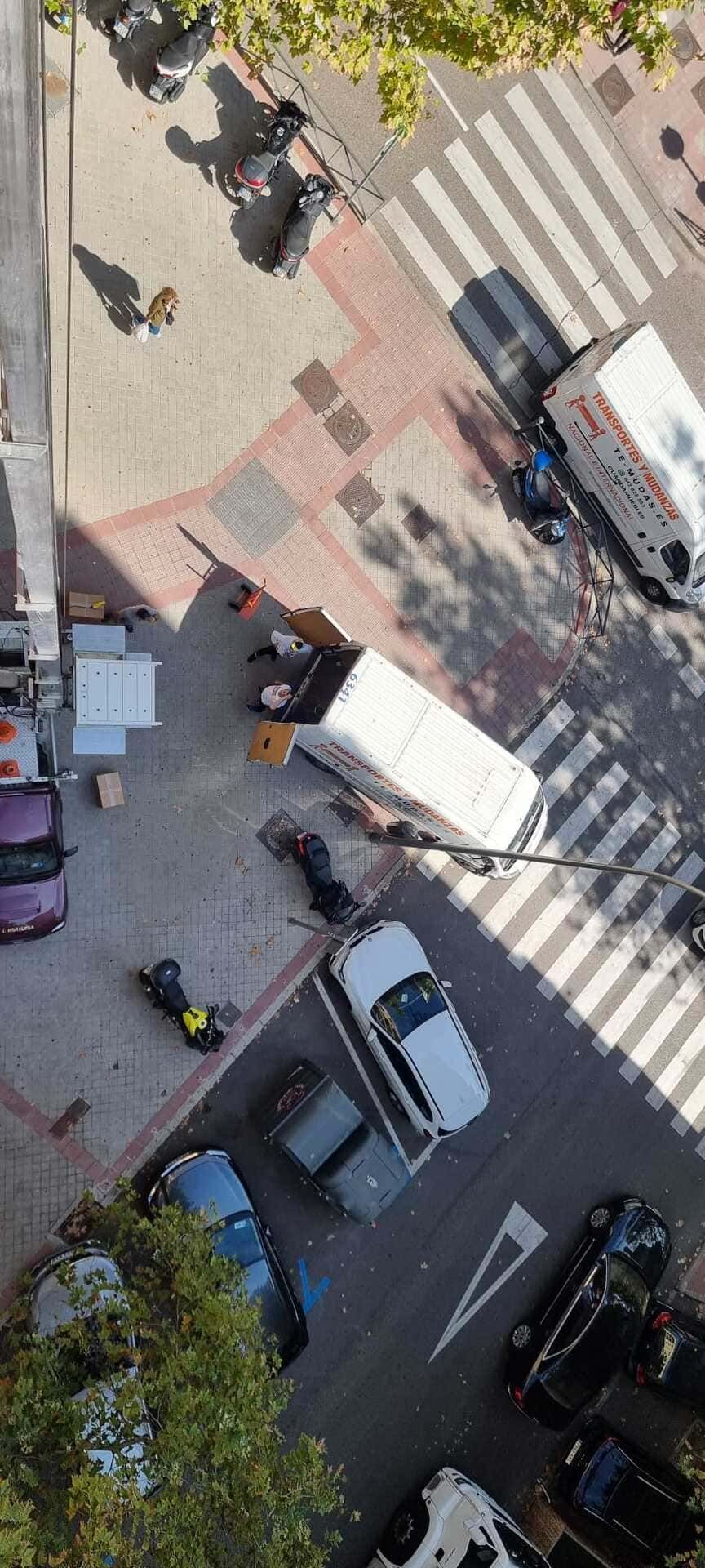 Vista aérea de una intersección de calles con coches, peatones, pasos de cebra y una furgoneta aparcada.