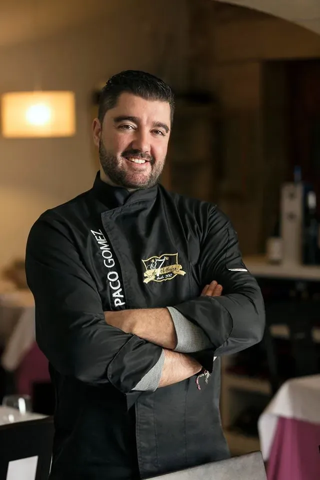 Un hombre con una chaqueta de chef está de pie en un restaurante con los brazos cruzados.