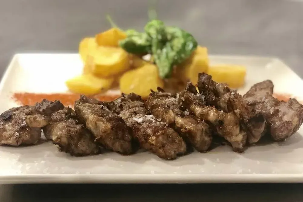 Un plato blanco cubierto con carne y patatas sobre una mesa.