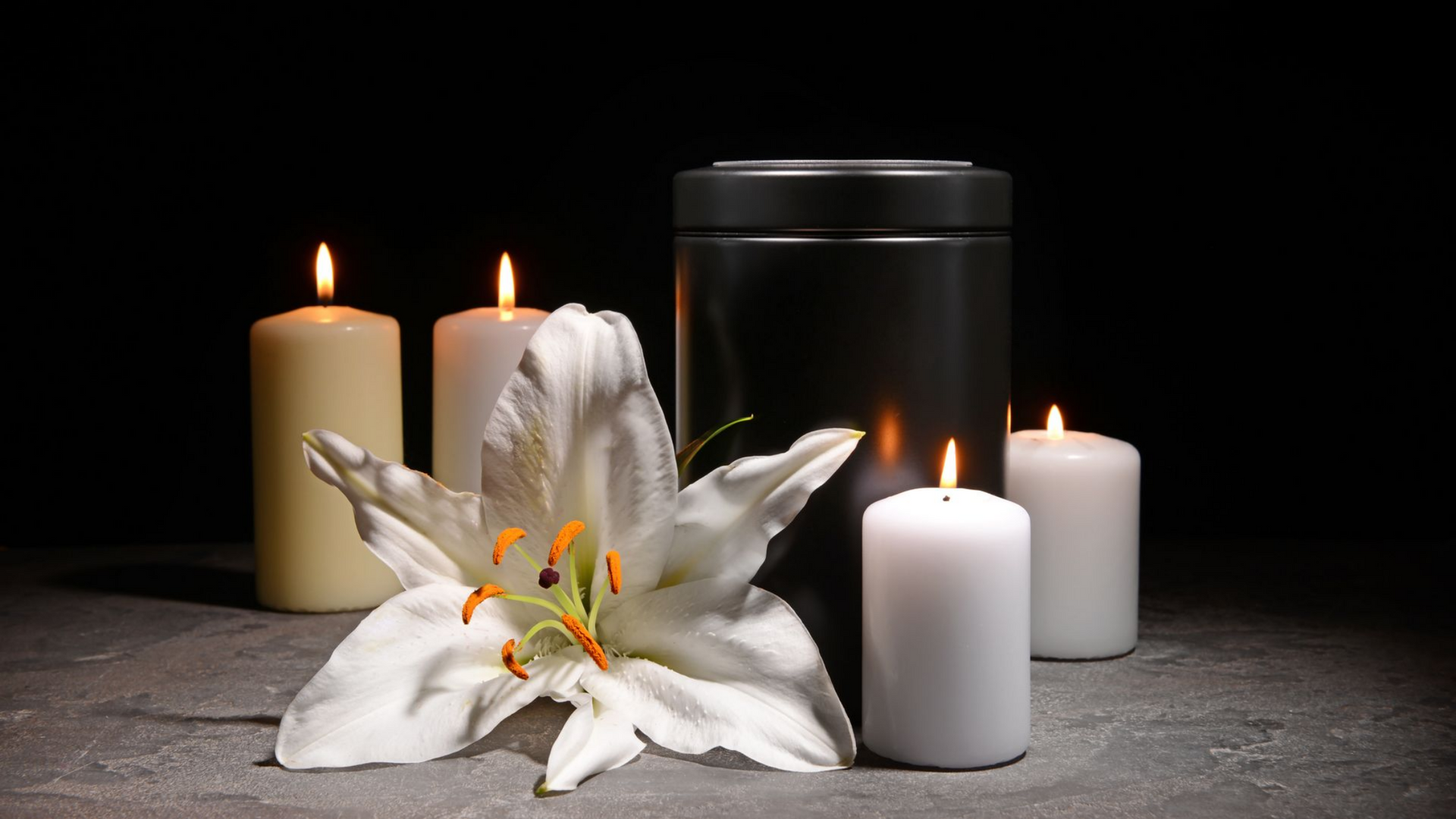 Un lys blanc et des bougies alumées autour d'une urne funéraire.