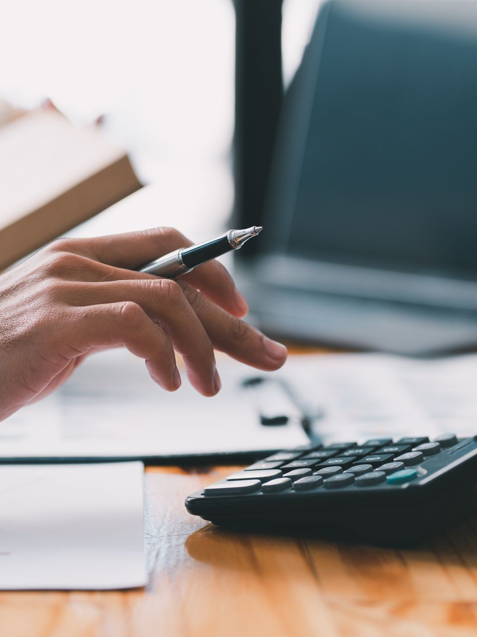 Main tenant un stylo au-dessus d'une calculatrice.