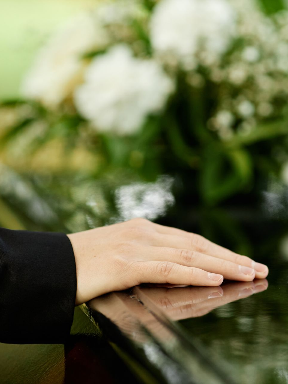 Une main posée sur un cercueil recouvert de fleurs.