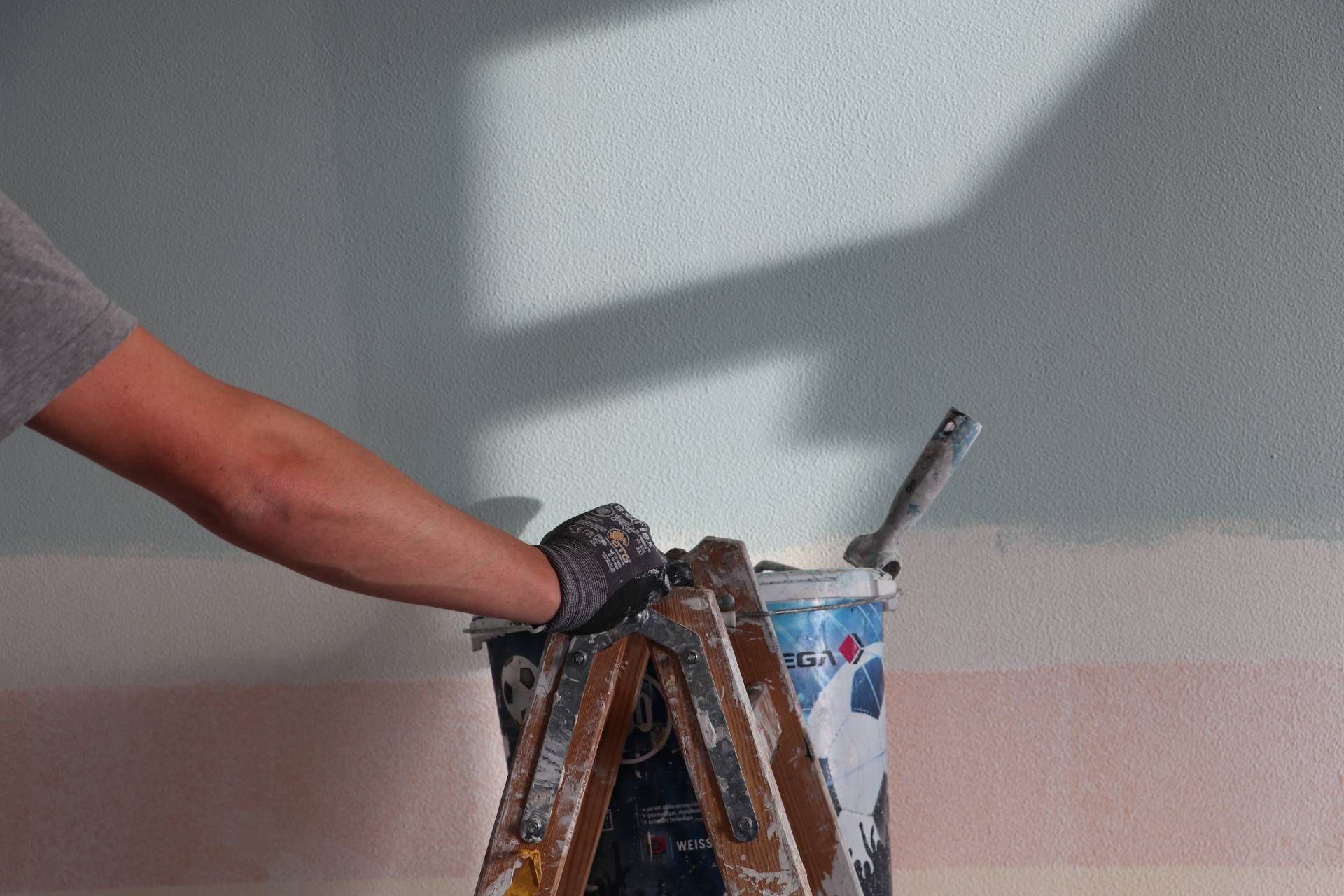 Eine Person hält eine Leiter neben einem Eimer Farbe.