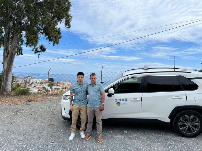 Dos hombres están parados junto a una camioneta blanca en un estacionamiento.