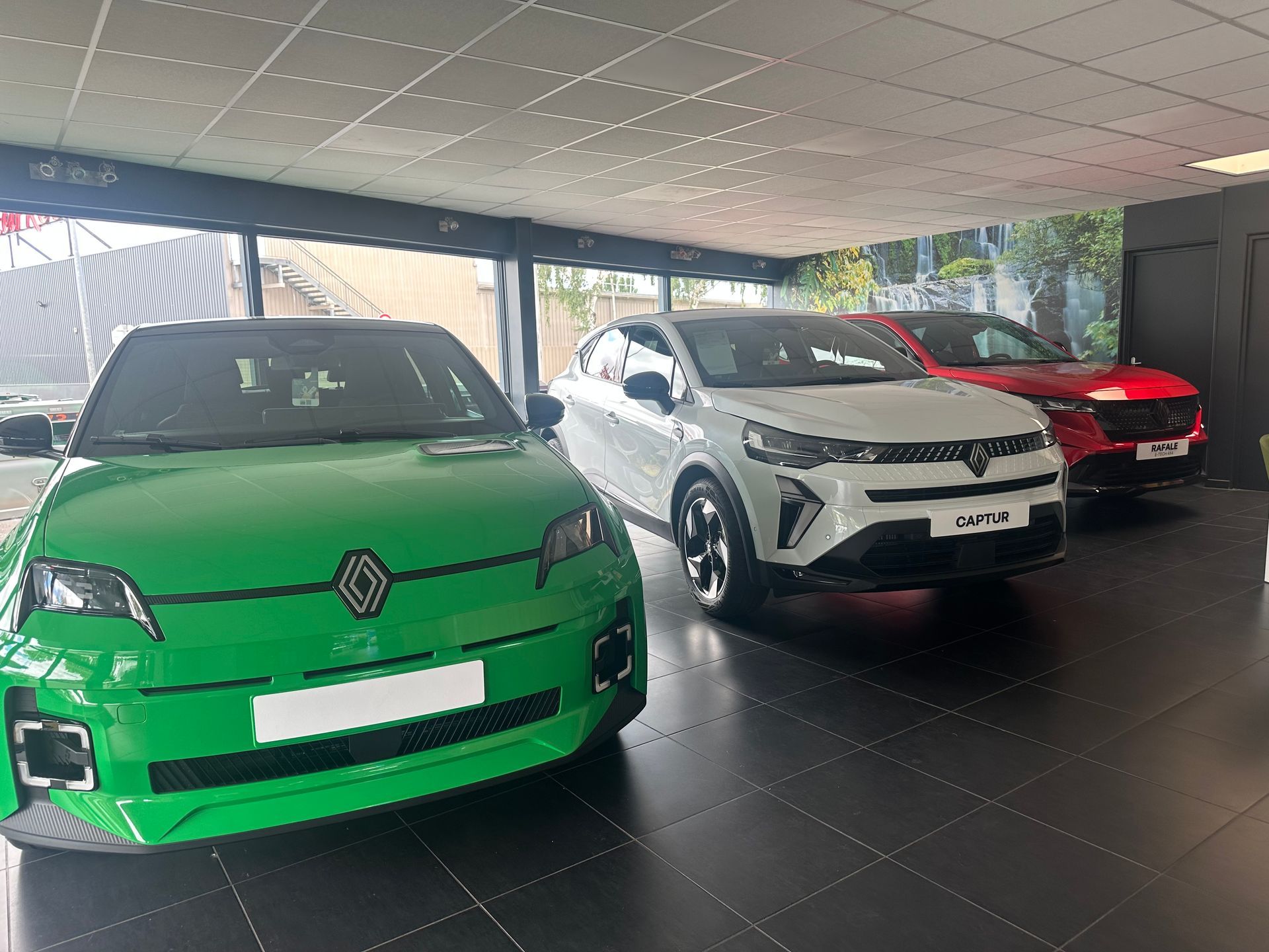 Des voitures vertes, blanches et rouges exposées dans un showroom aux grandes vitrines et au sol noir.