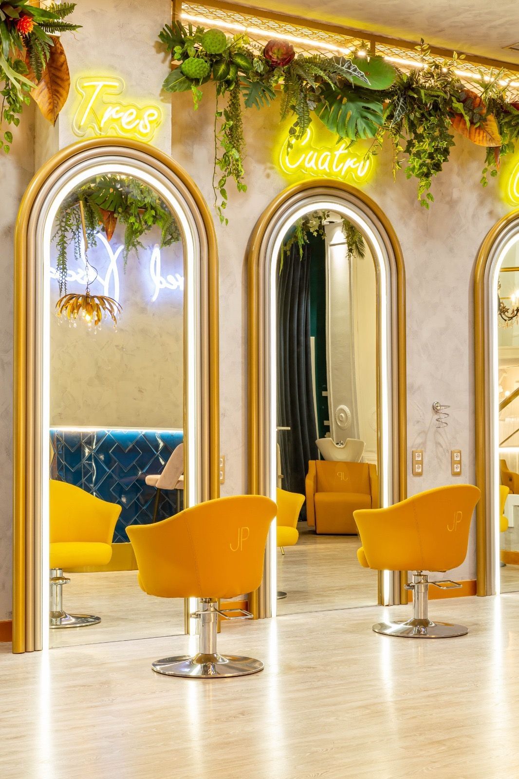 Interior de peluquería con sillas amarillas, espejos arqueados y letreros de neón.