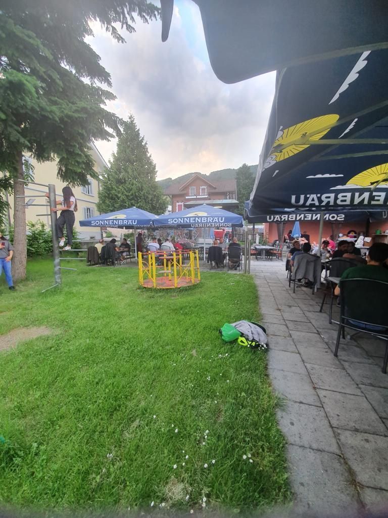 Eine Gruppe von Menschen sitzt unter Sonnenschirmen in einem Park.