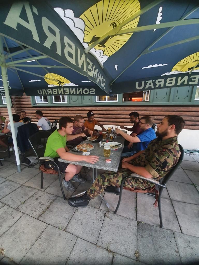 Eine Gruppe von Männern sitzt an Tischen unter einem Schirm mit der Aufschrift „uaavis“