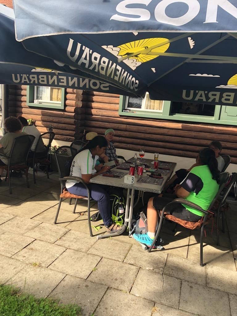 Eine Gruppe von Menschen sitzt unter Sonnenschirmen an Tischen vor einem Restaurant.