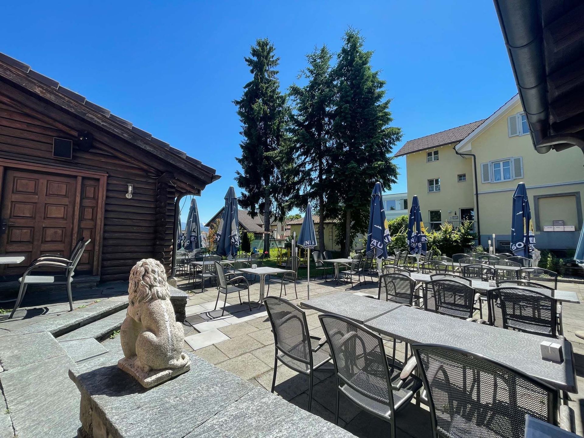 In der Mitte einer Terrasse mit Tischen und Stühlen steht eine Löwenstatue.