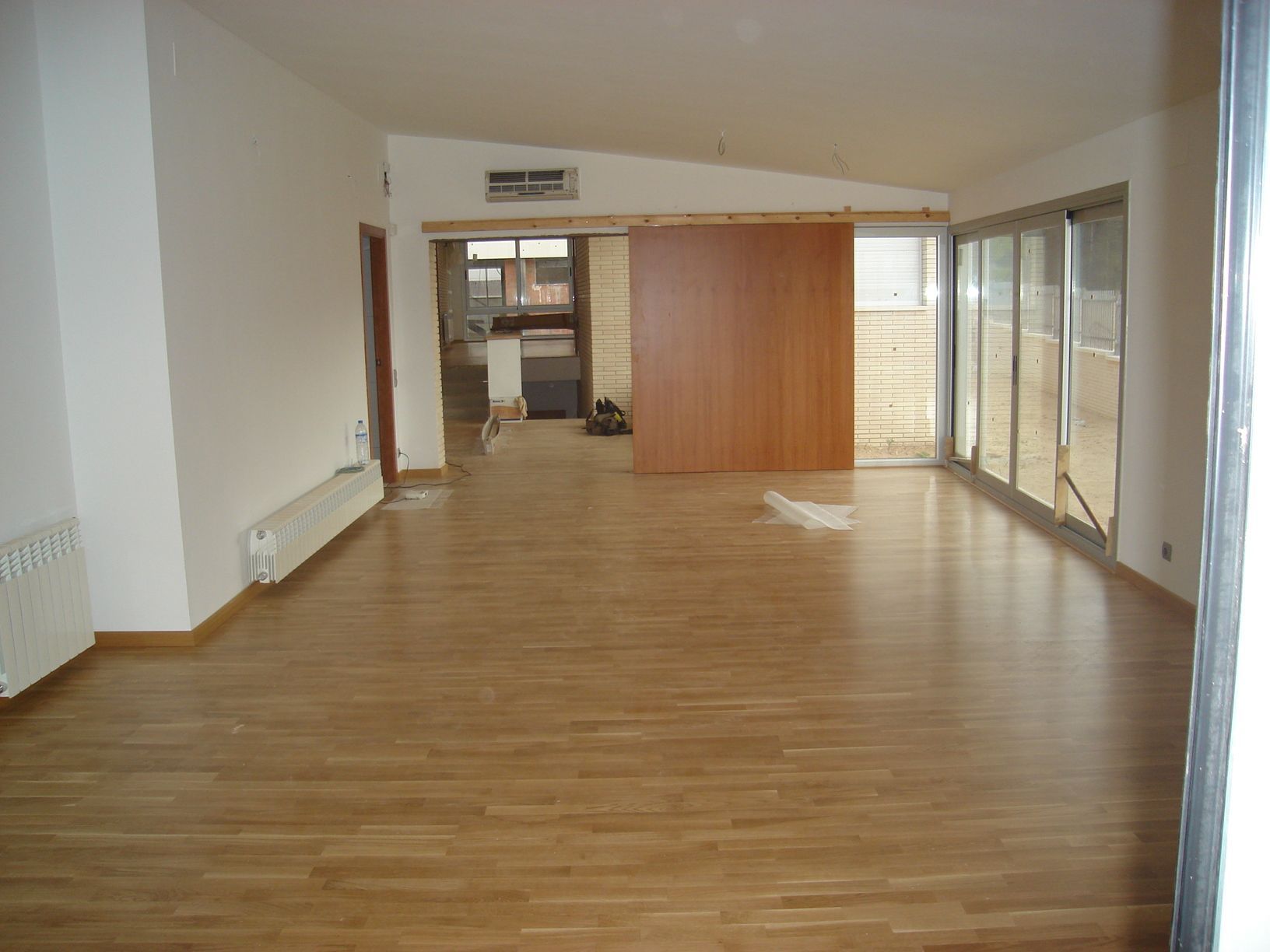 Una gran habitación vacía con pisos de madera y puertas corredizas de vidrio.