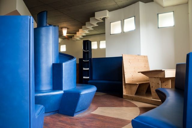 Modernes Interieur mit blauen, geometrischen Sitzmöbeln und Holztischen unter kleinen Fenstern
