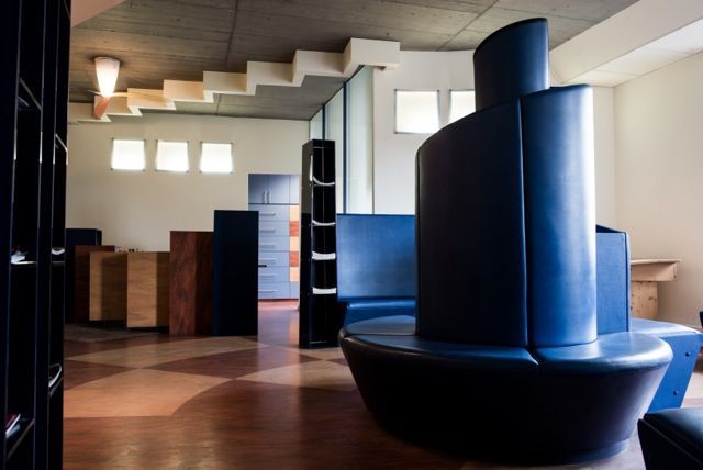 Modernes Interieur mit blauen, skulpturalen Sitzmöbeln, Holzboden und einer Treppe im Hintergrund
