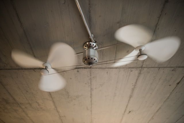 Dreiflügeliger Deckenventilator mit Beleuchtung an einer Betondecke, von unten gesehen