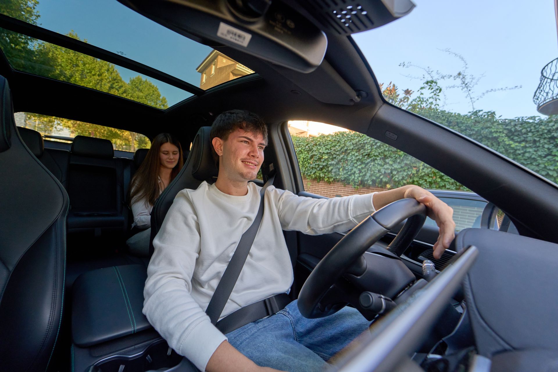 Personne conduisant une voiture avec un passager à l'arrière, toit ouvrant ouvert, vue intérieure.