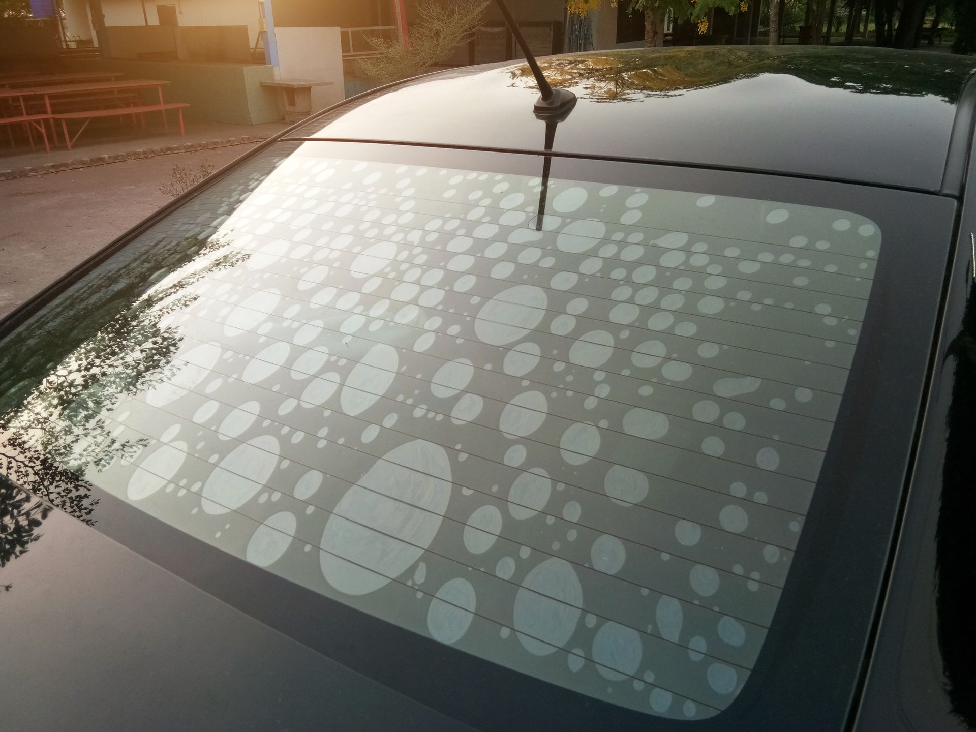 Lunette arrière de voiture recouverte d'un motif dépoli de points ovales.