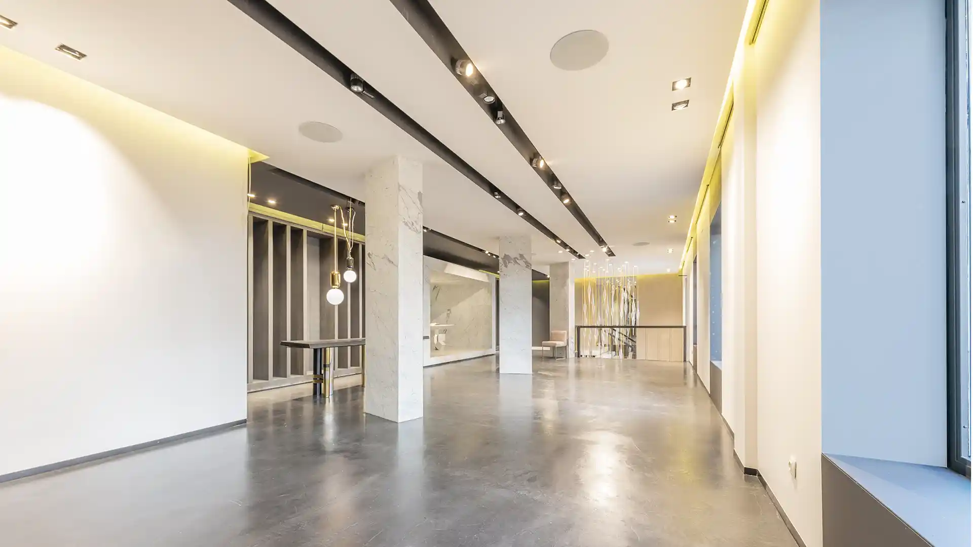 Interior luminoso y moderno con paredes blancas, suelo de hormigón pulido e iluminación lineal.