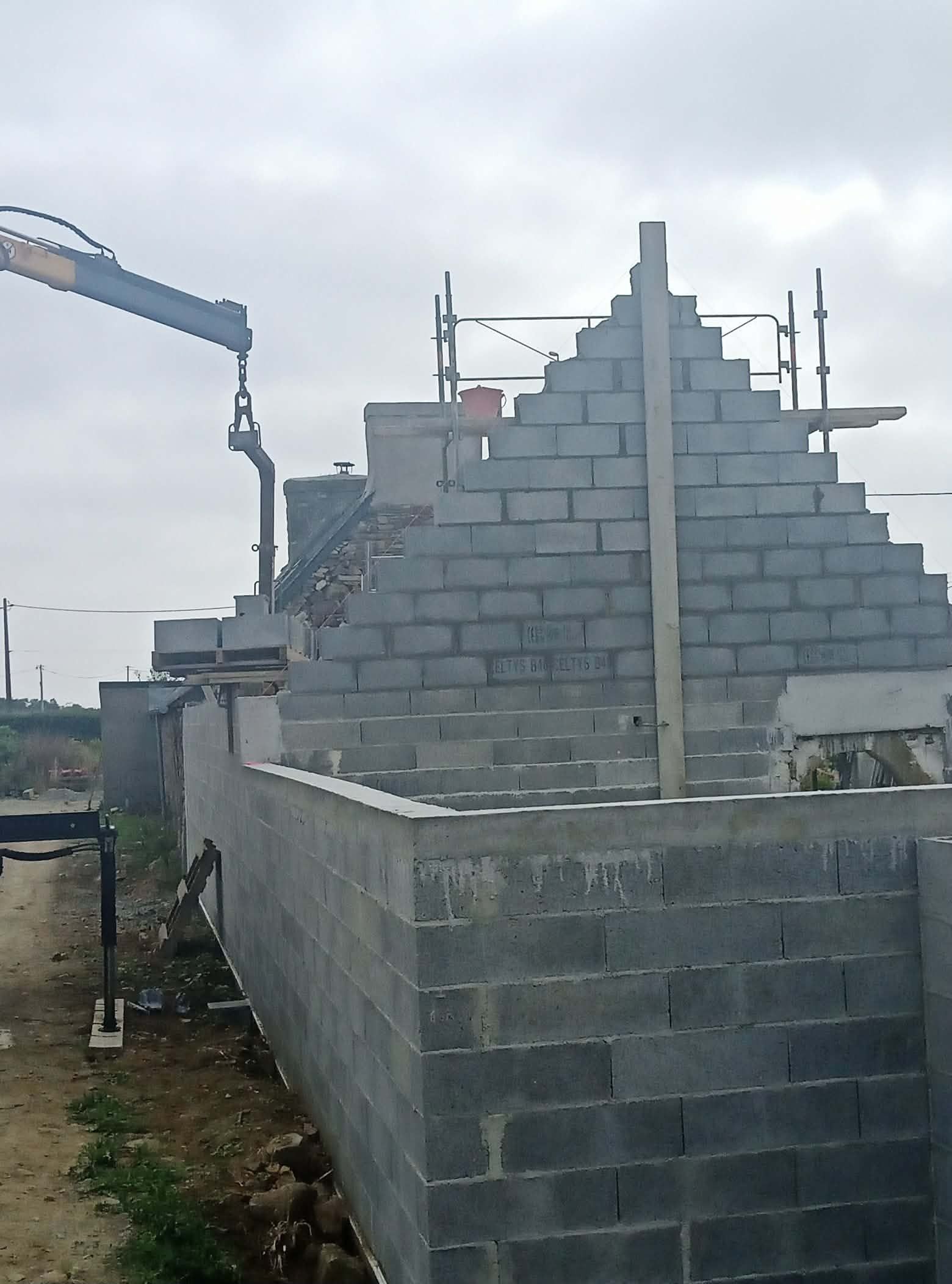 Maison en parpaings partiellement construite, avec un toit à gradins inachevé.