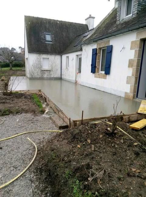 Cour inondée à côté d'une maison aux volets et au premier plan boueux.