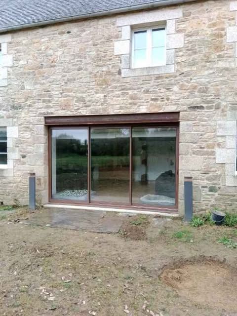Maison en pierre avec de grandes portes coulissantes en verre et une petite fenêtre au-dessus.