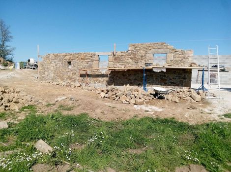 Bâtiment en pierre en construction, avec des échelles, des gravats.
