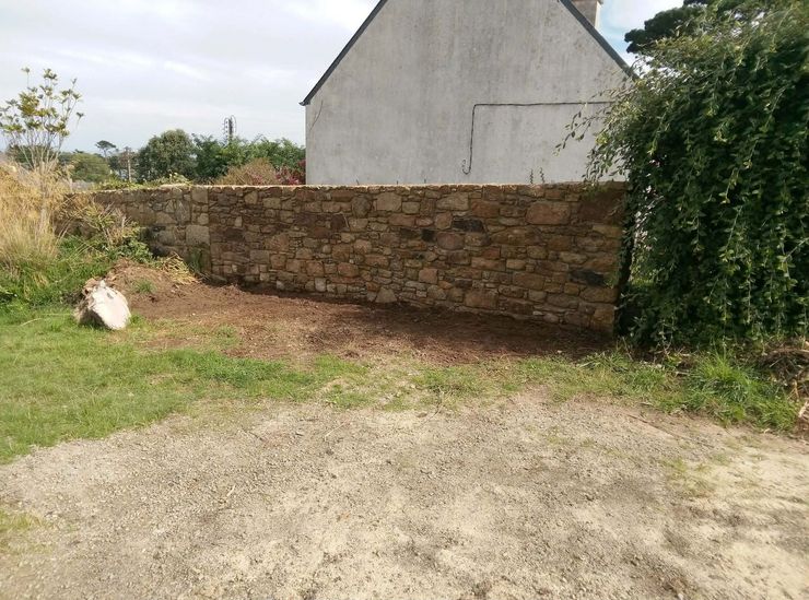 Mur de pierre à côté d'une maison, avec une cour et un premier plan de gravier.