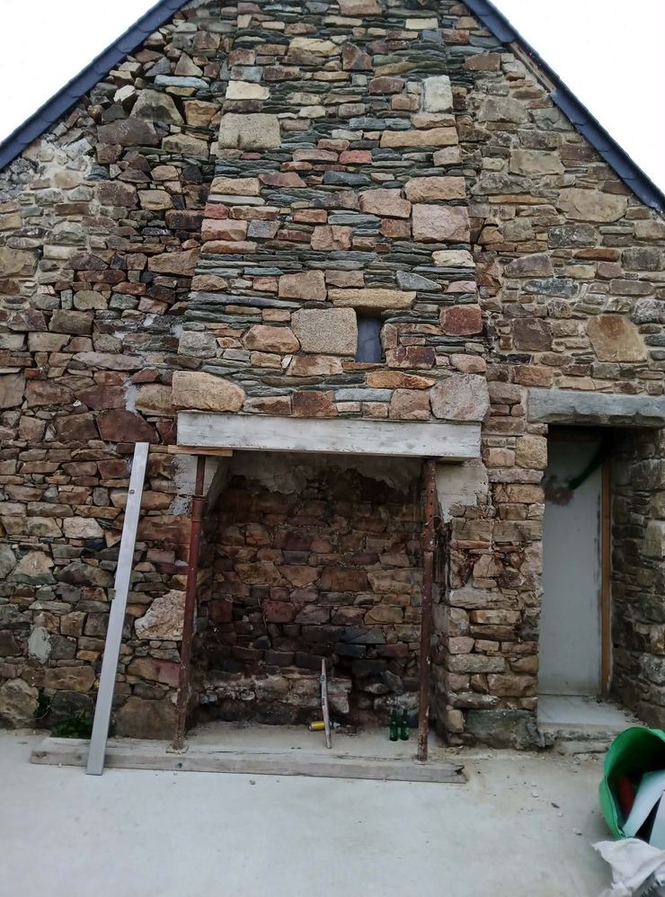 Façade en pierre avec une petite porte ouverte et un mur en maçonnerie brute.