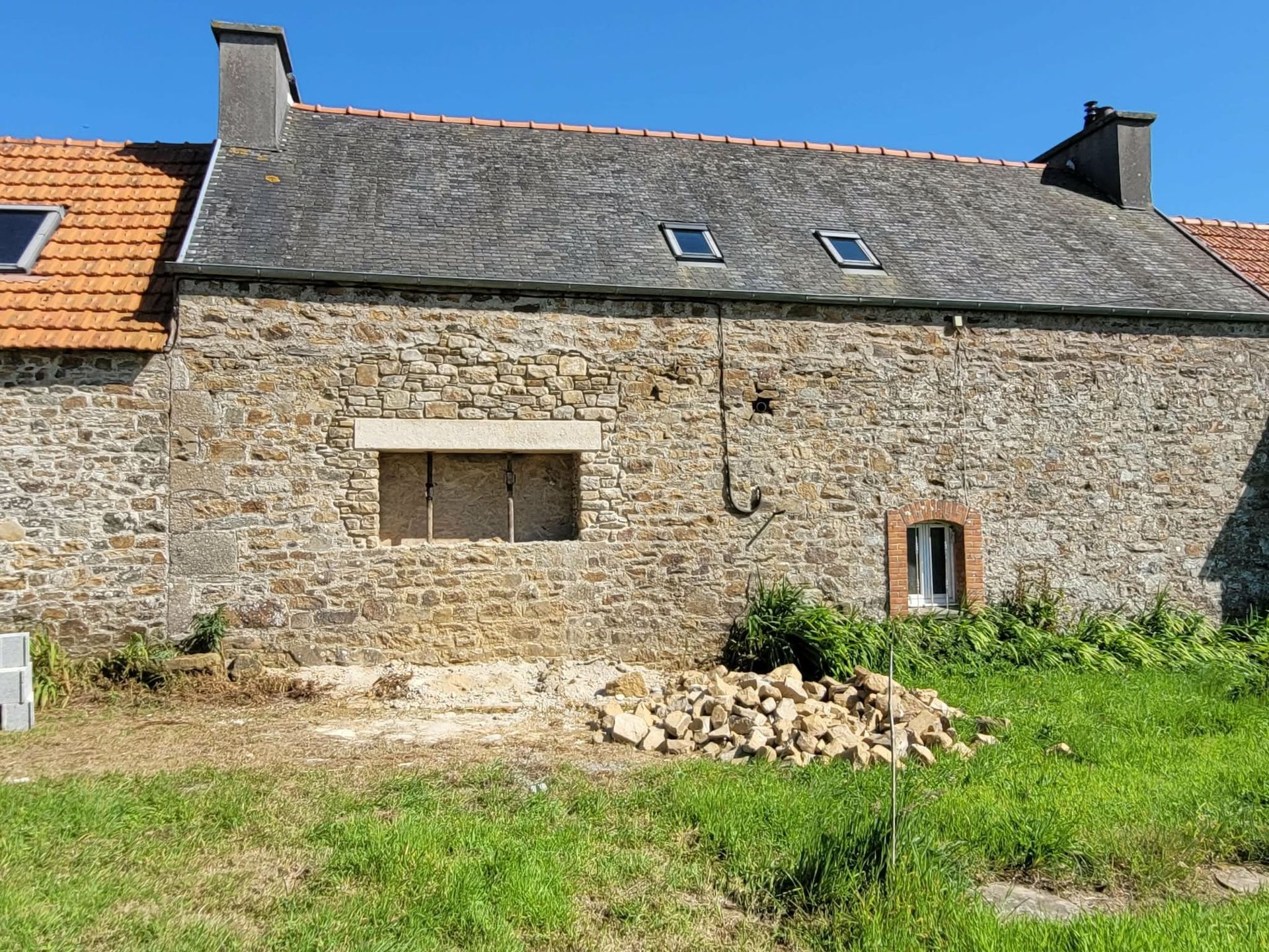 Maisonnette en pierre au toit d'ardoise, petites fenêtres et cour gazonnée.